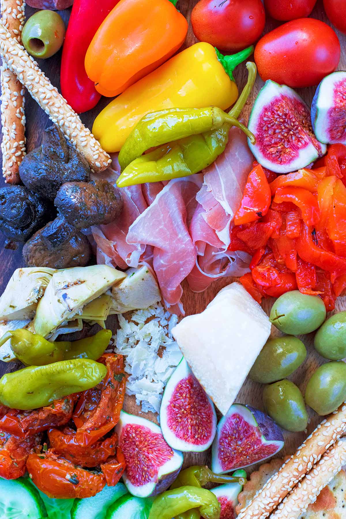 Meats, bread, olives, figs, cheese peppers and mushrooms on a wooden board.