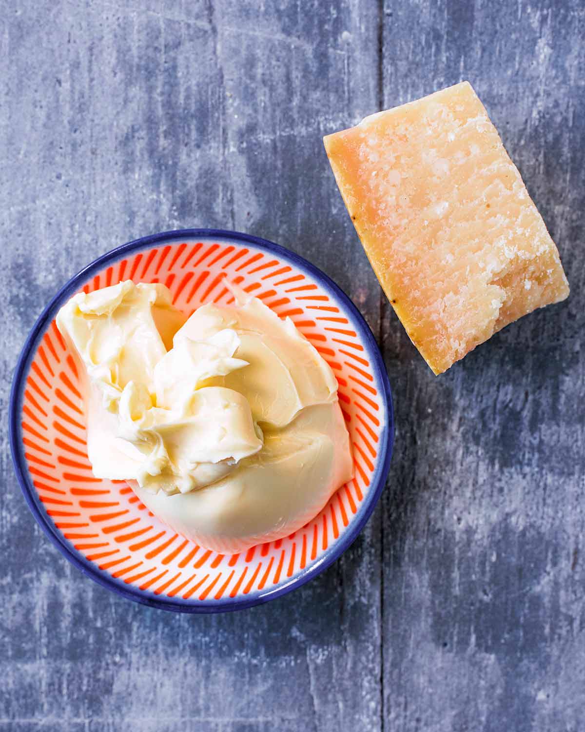 A small dish with a dollop of cream cheese next to a small block of hard cheese.
