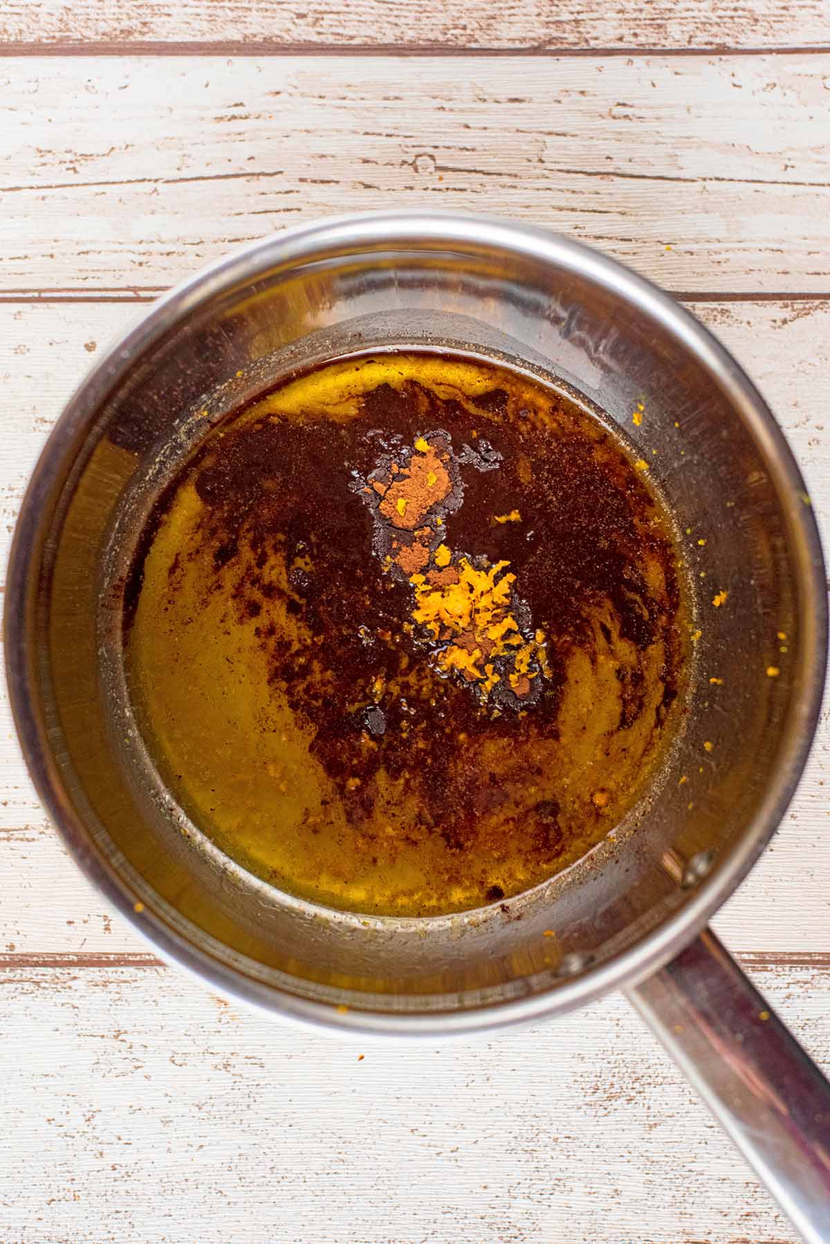 A stainless steel saucepan containing melted butter, golden syrup, spices and orange zest.