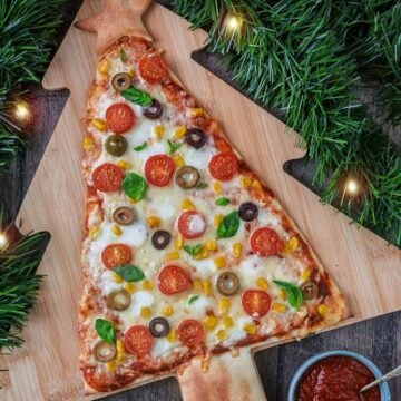 A Christmas tree shaped pizza on a Christmas tree shaped wooden board.