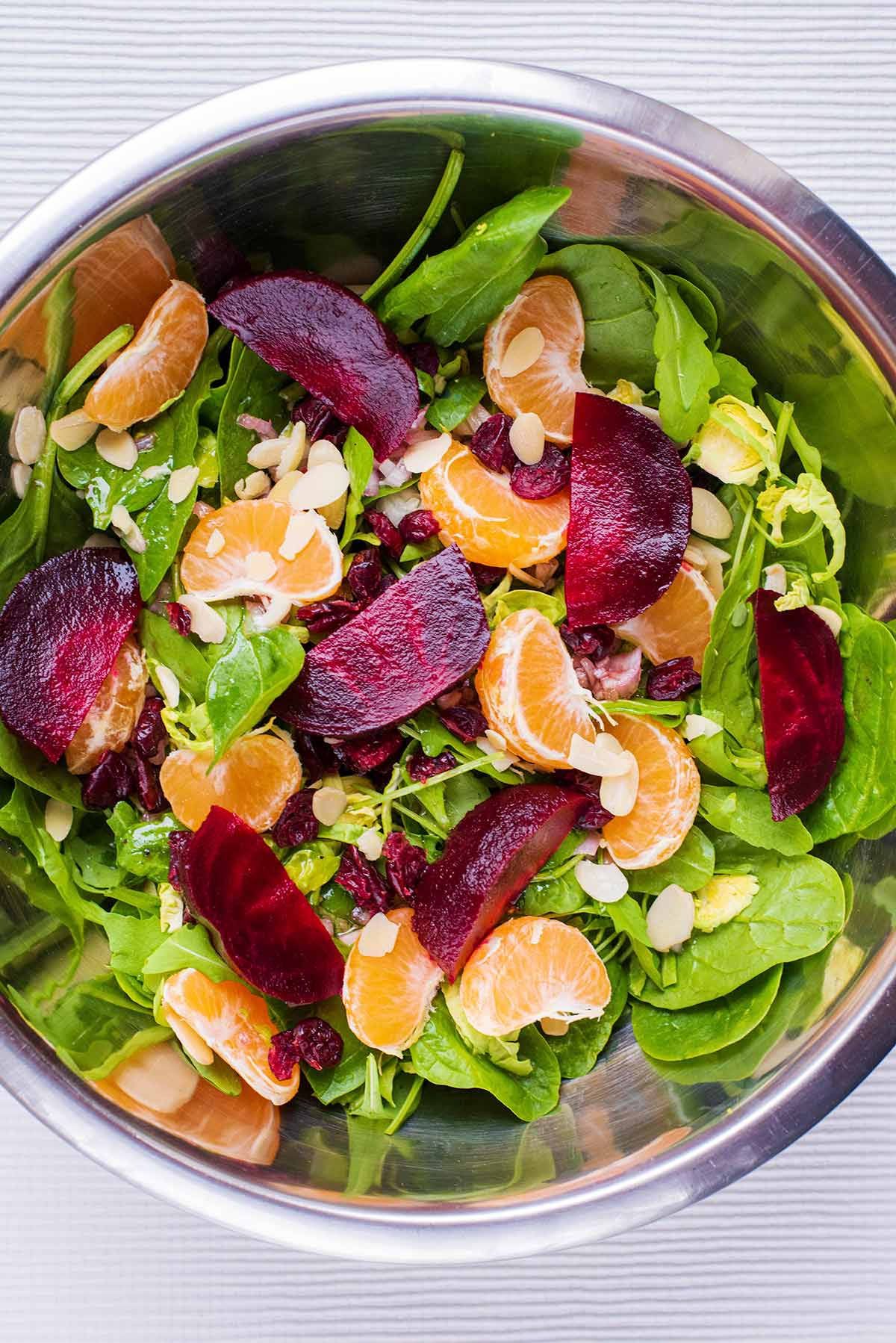 A large metal bowl containing salad leaves, clementine segments and beetroot chunks.