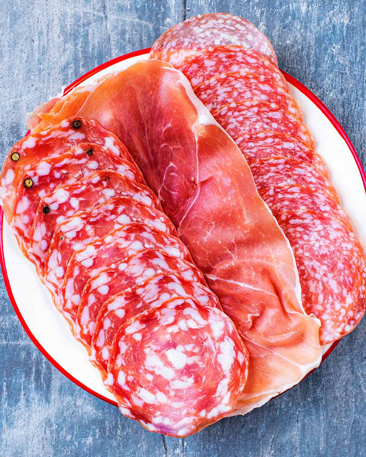 A selection of three cured meats on a white plate.