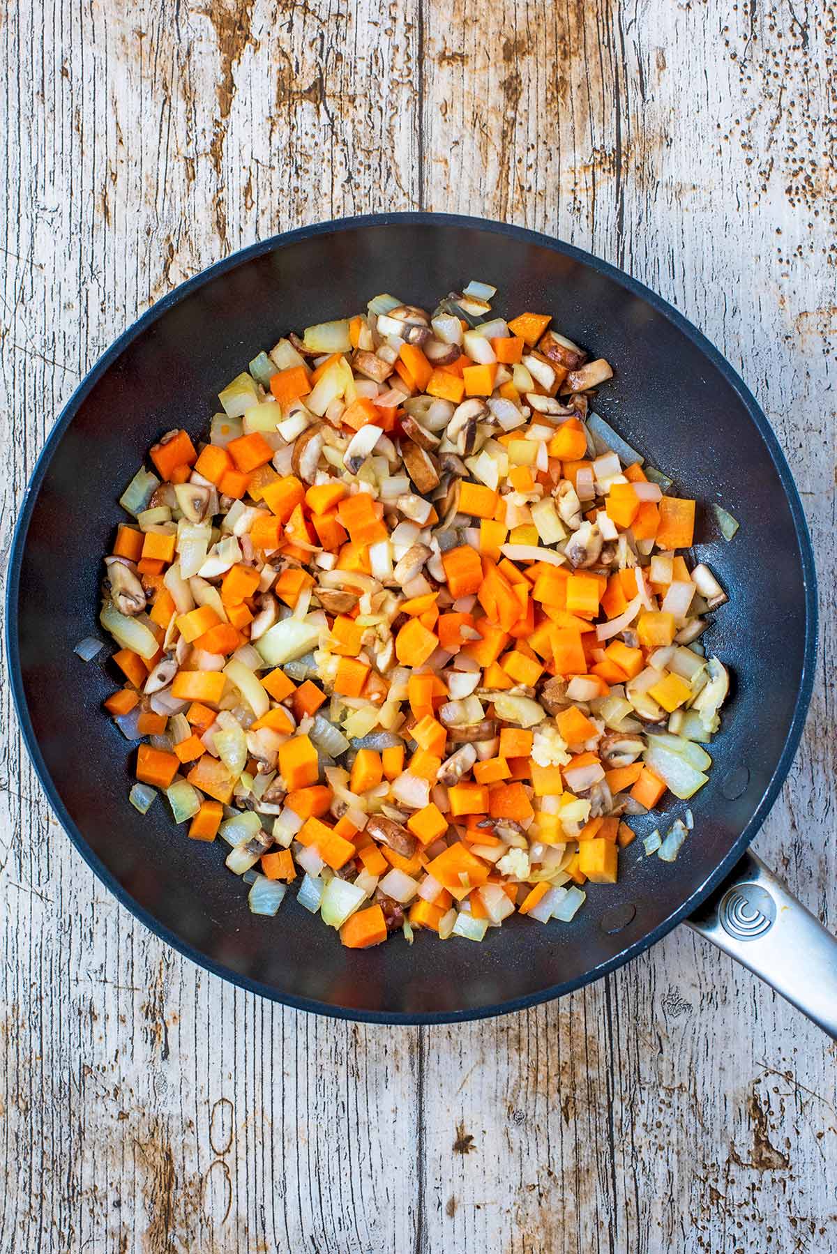 A frying pan with chopped carrot, onion, mushrooms and garlic.