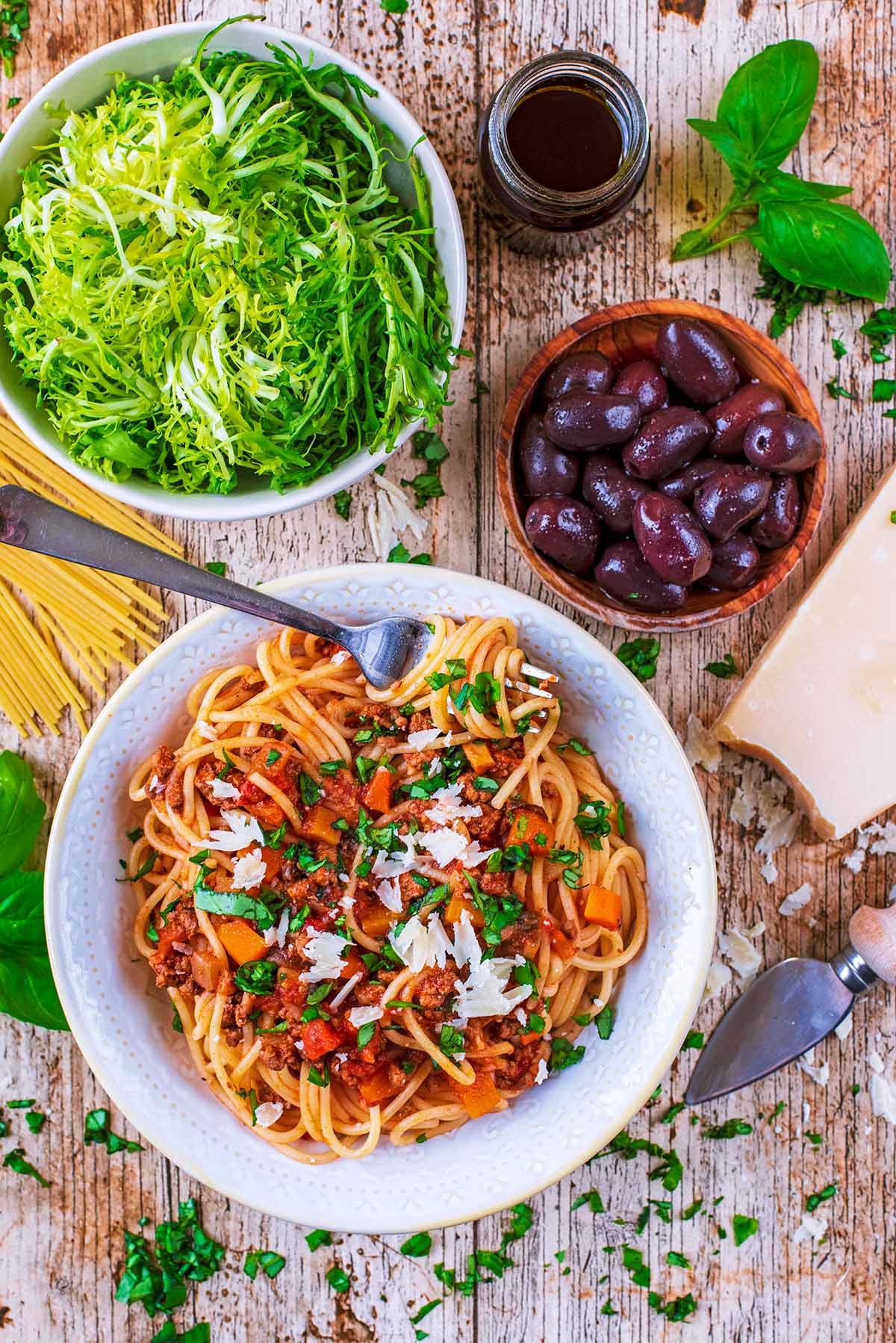 Spaghetti Bolognese with a bowl of salad and some black olives.