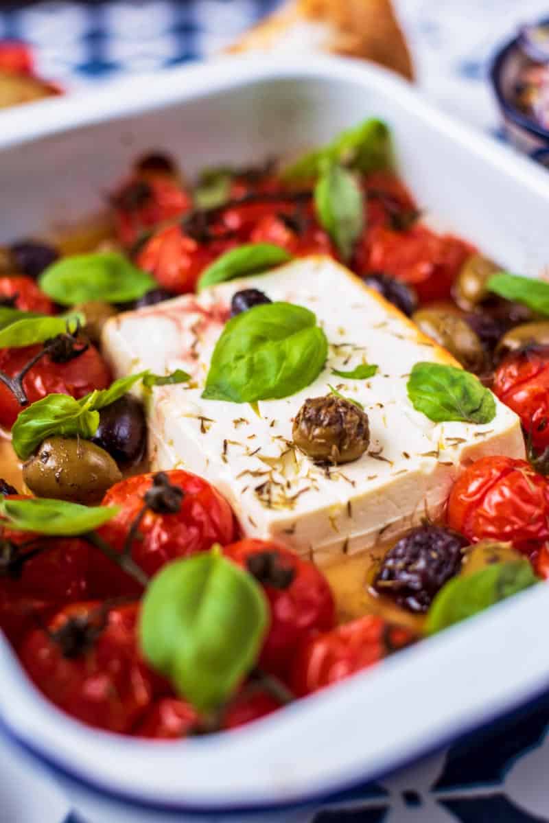 Feta cheese, tomatoes, olives and basil in a white baking tray.