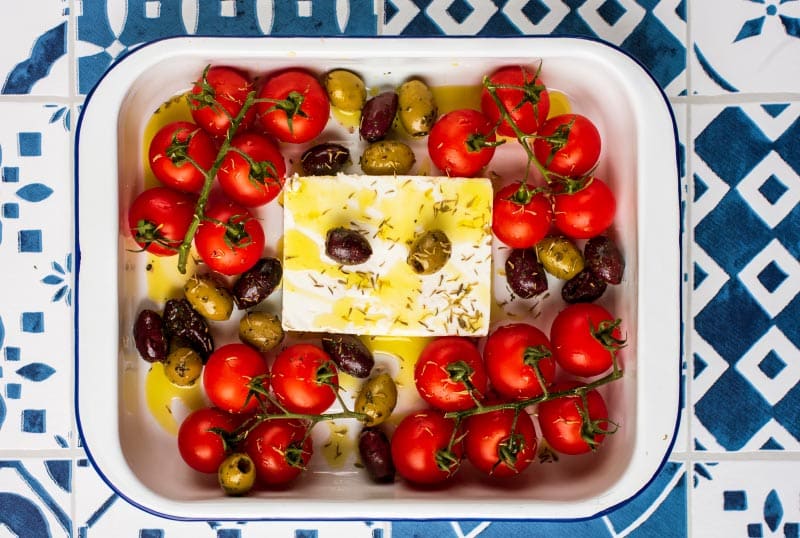 Feta, tomatoes and olives in a baking dish. Oil has been drizzled over everything.