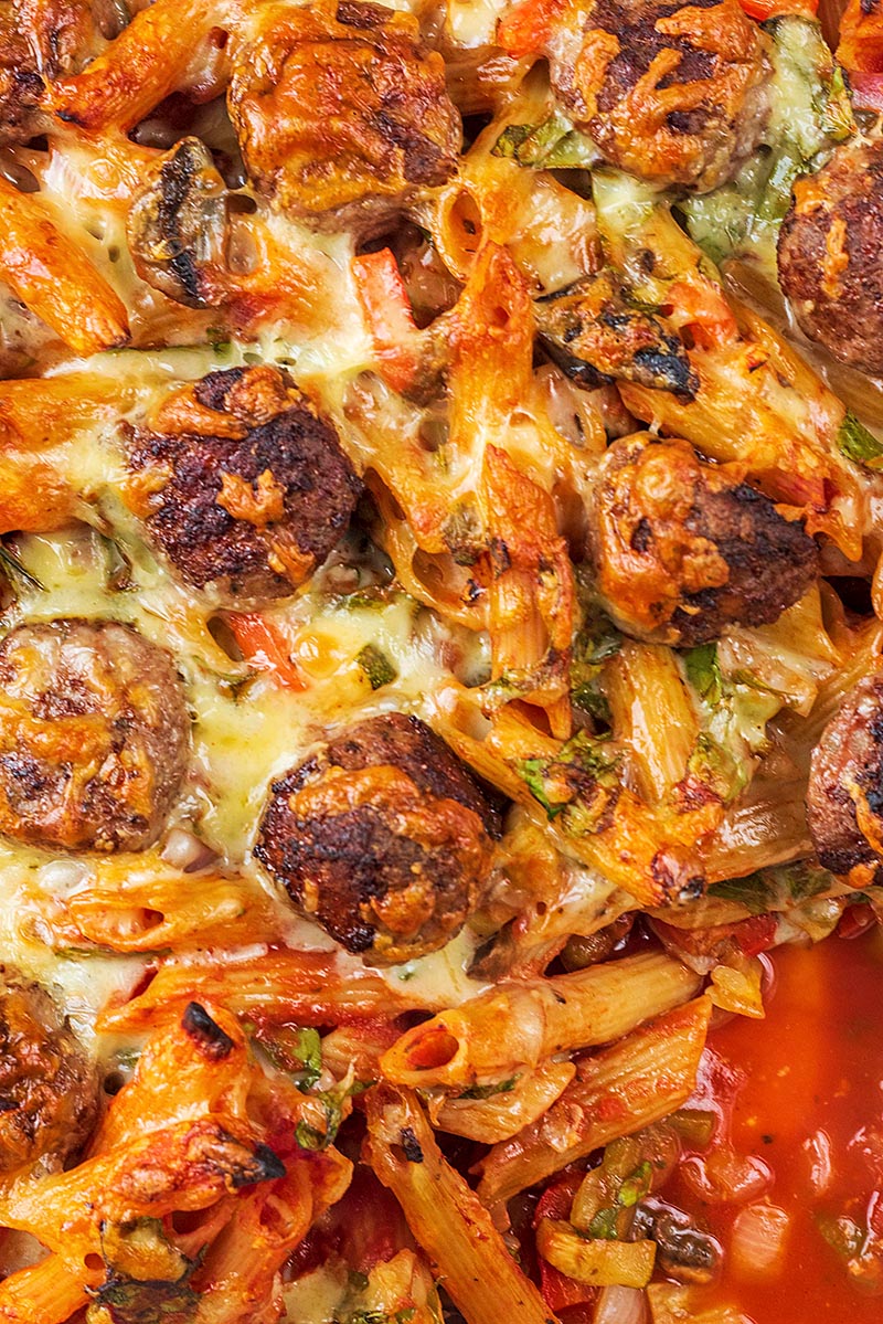 Meatballs and penne pasta in a tomato sauce covered in melted cheese.
