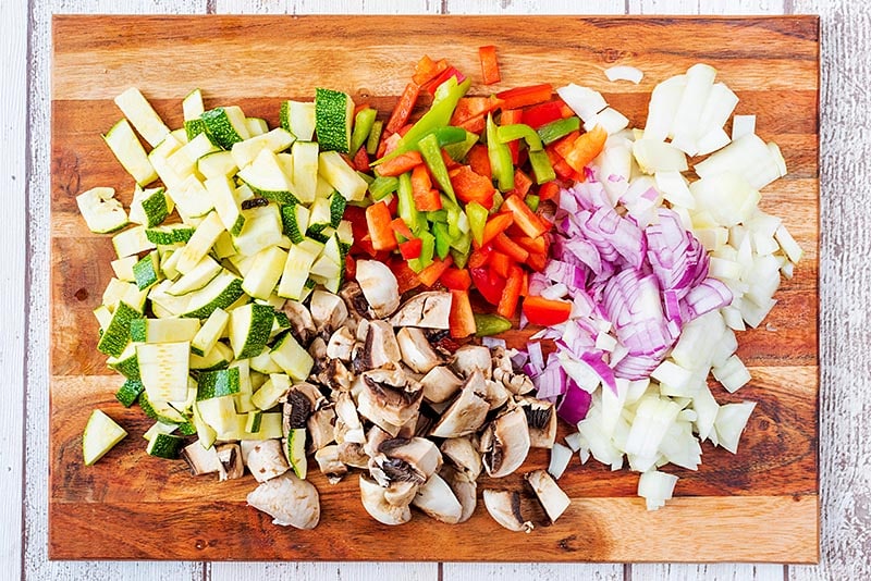 A wooden chopping board covered with chopped vegetables.
