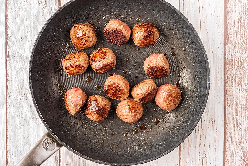 A frying pan with twelve meatballs in it.