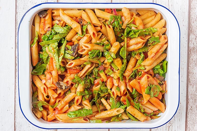 A large rectangular baking dish containing cooked pasta and chopped vegetables all in a tomato sauce.
