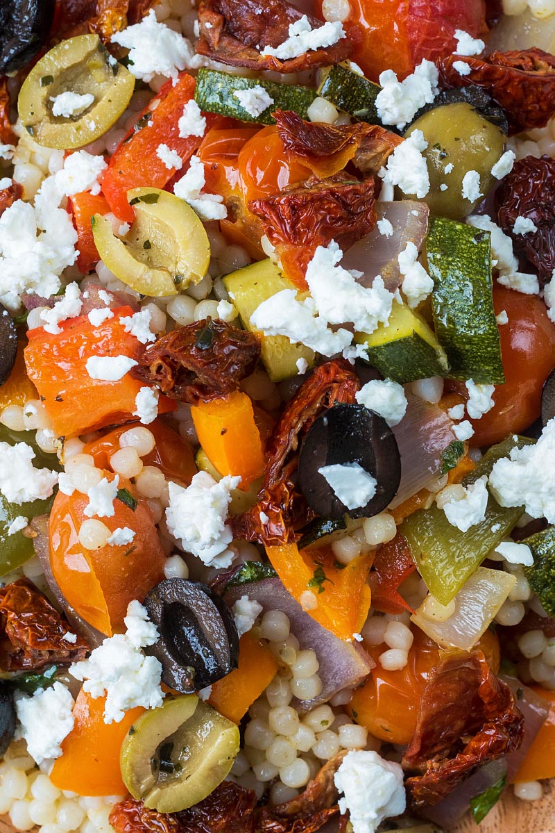 Olives and feta cheese on top of giant couscous salad with roasted vegetables.