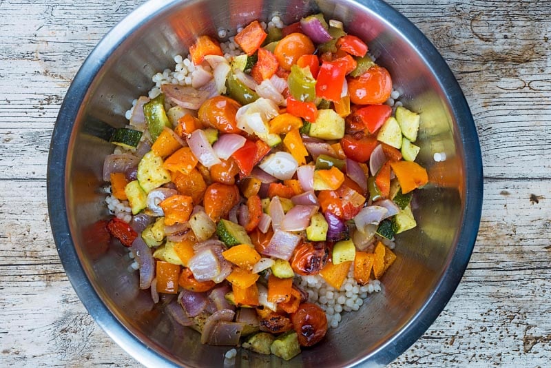 A large mixing bowl containing giant couscous and roasted vegetables.