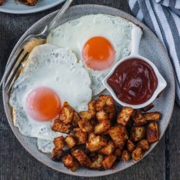 Crispy baked breakfast potatoes on a plate with two fried eggs.