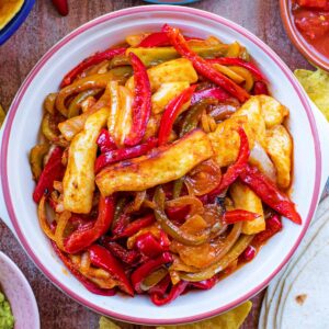 A serving bowl of Halloumi Fajita filling surrounded by flour tortillas, guacamole, salsa and refried beans.