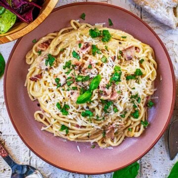 A bowl of healthy carbonara with small basil leaves on top.