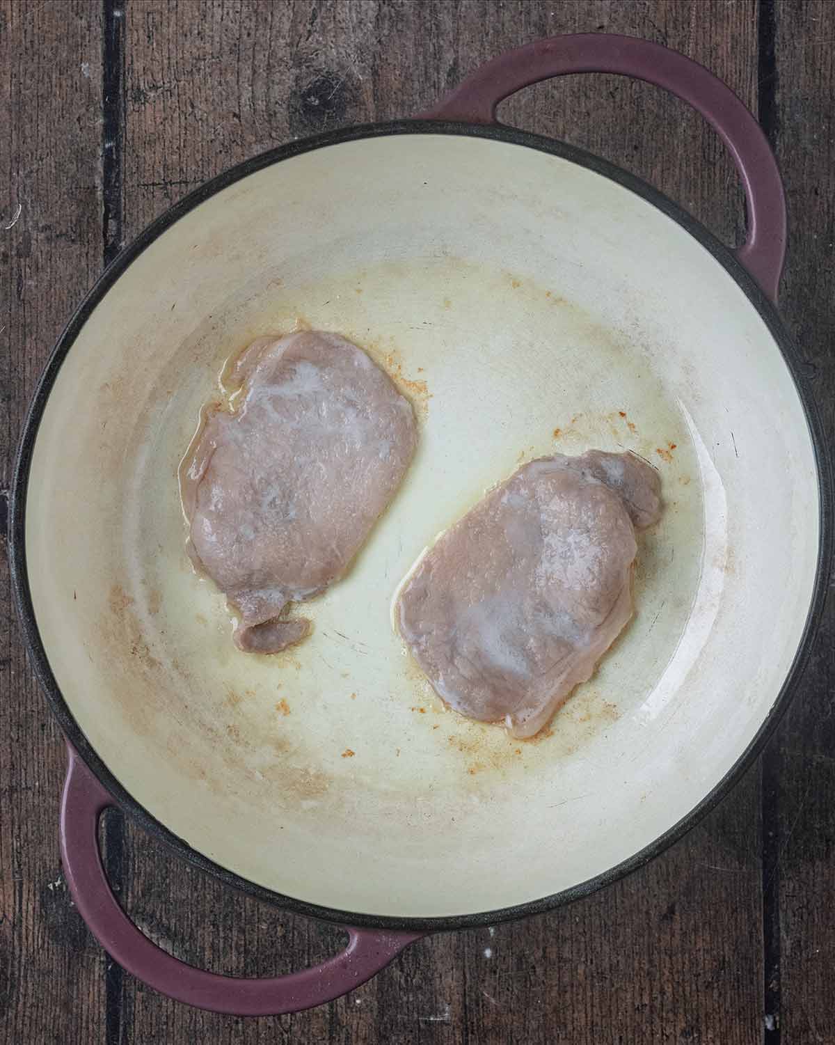 Two rashers of bacon cooking in a large pan.