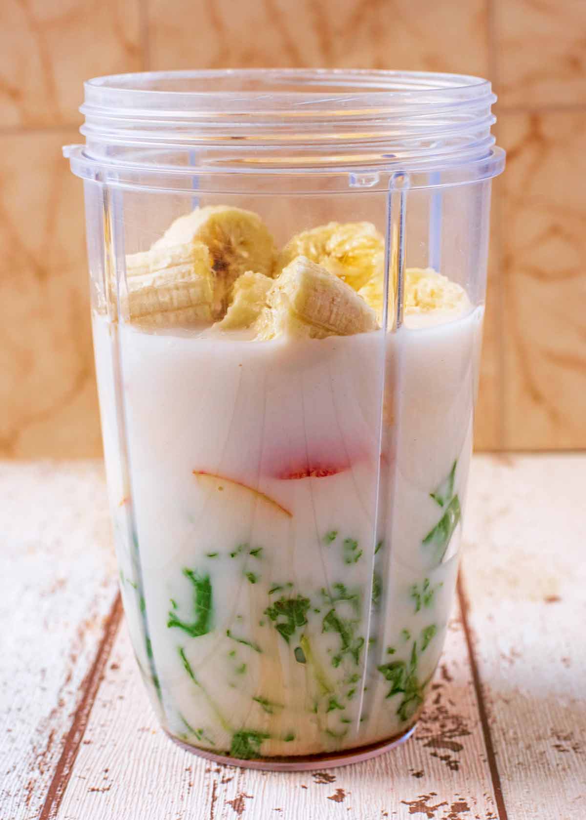 Milk, fruit and kale in a blender jug.