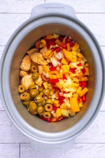 A slow cooker pot containing chicken, chorizo and chopped vegetables.