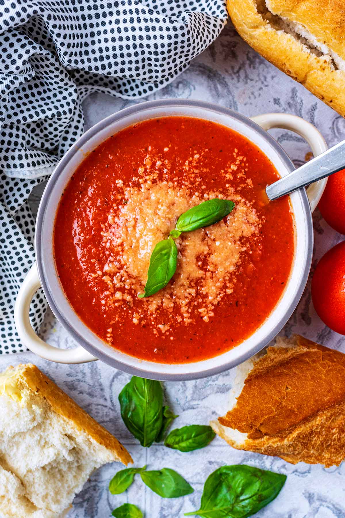 A bowl of tomato soup topped with grated cheese and basil leaves.