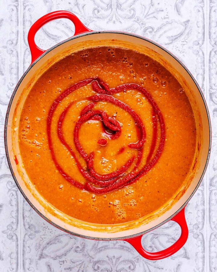 A large red pot containing tomato soup and tomato puree.
