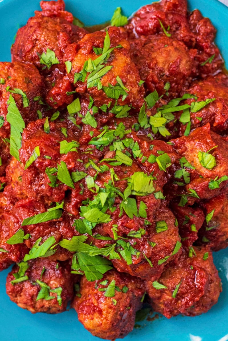 A plate of meatballs in a tomato sauce topped with chopped herbs.