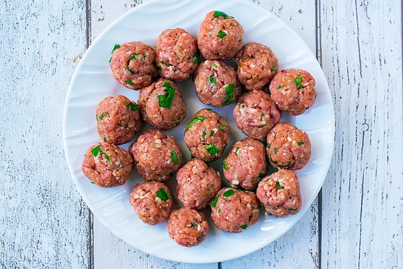 A plate with raw meatballs on it.