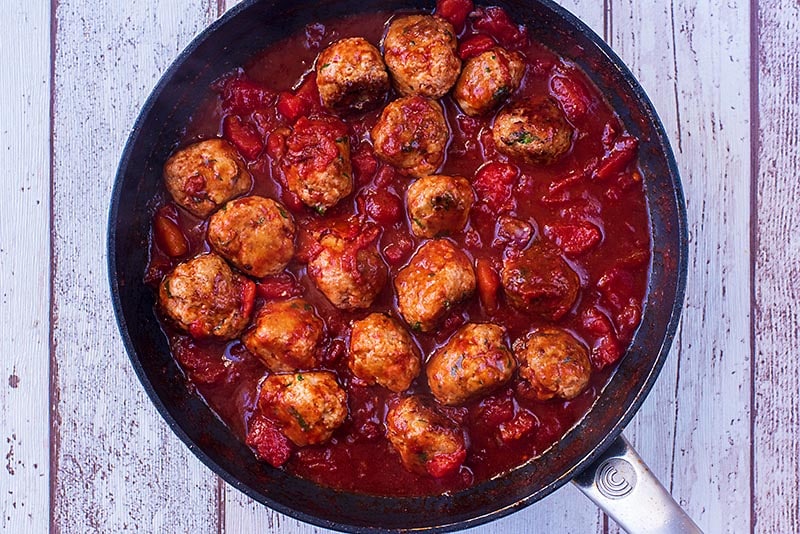 A frying pan with meatballs cooking in a tomato sauce.