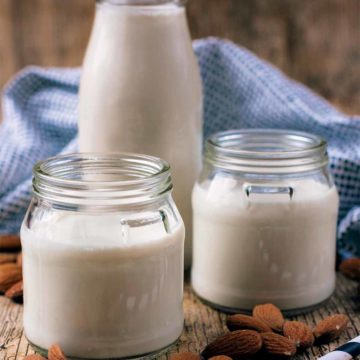 Two small jars of almost milk in front of a tall bottle of almond milk.