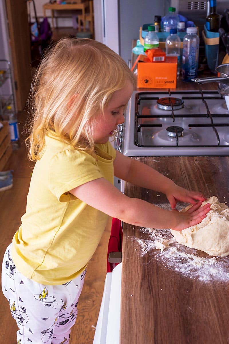 A toddler stood at a work surface kneading dough.