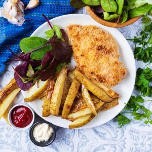 A chicken Kiev on a plate with salad and fries.