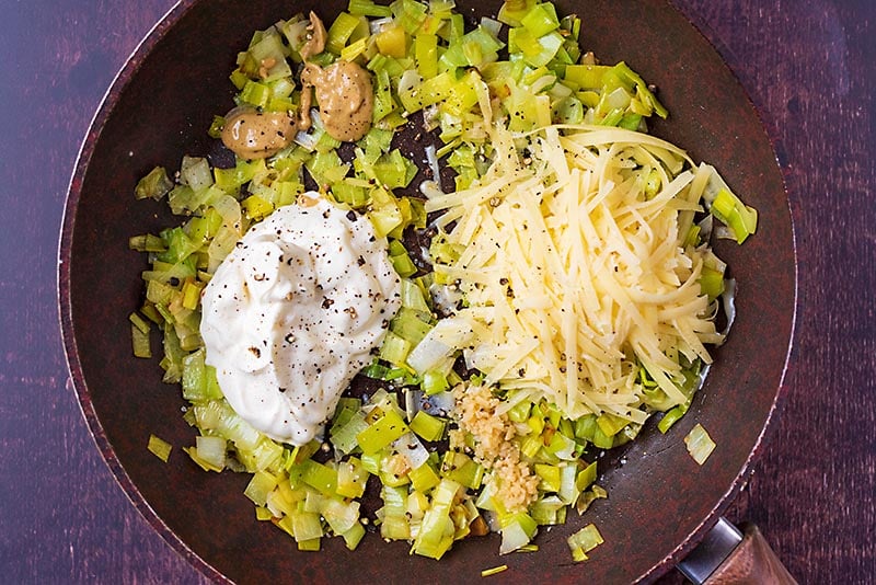 A frying pan with cooked leeks, a dollop of creme fraiche, grated cheese and some mustard.