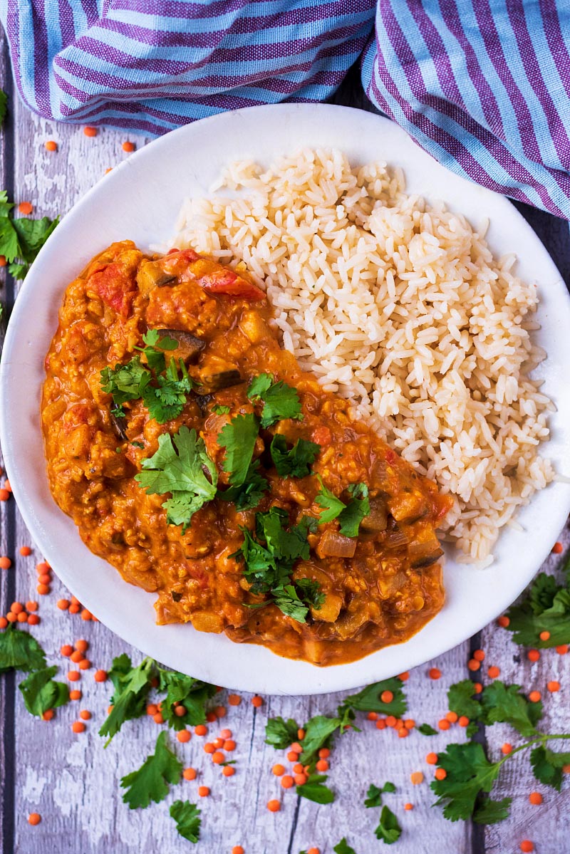 A bowl of lentil curry and rice next to a striped towel.