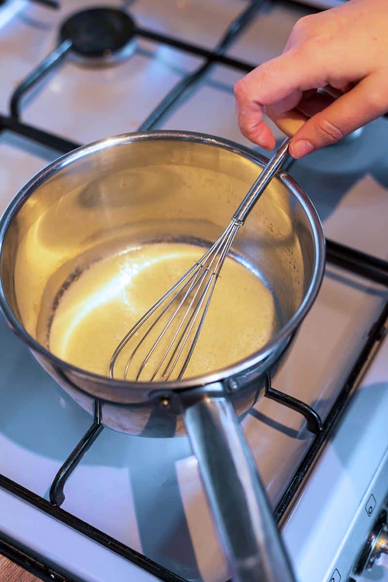 Oil and flour being whisked in a saucepan.