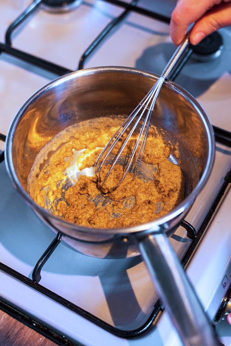 A brown paste being whisked in a saucepan.