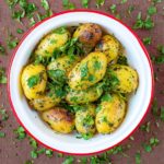 A bowl of Four Herb Roasted Potatoes in a red rimmed white bowl