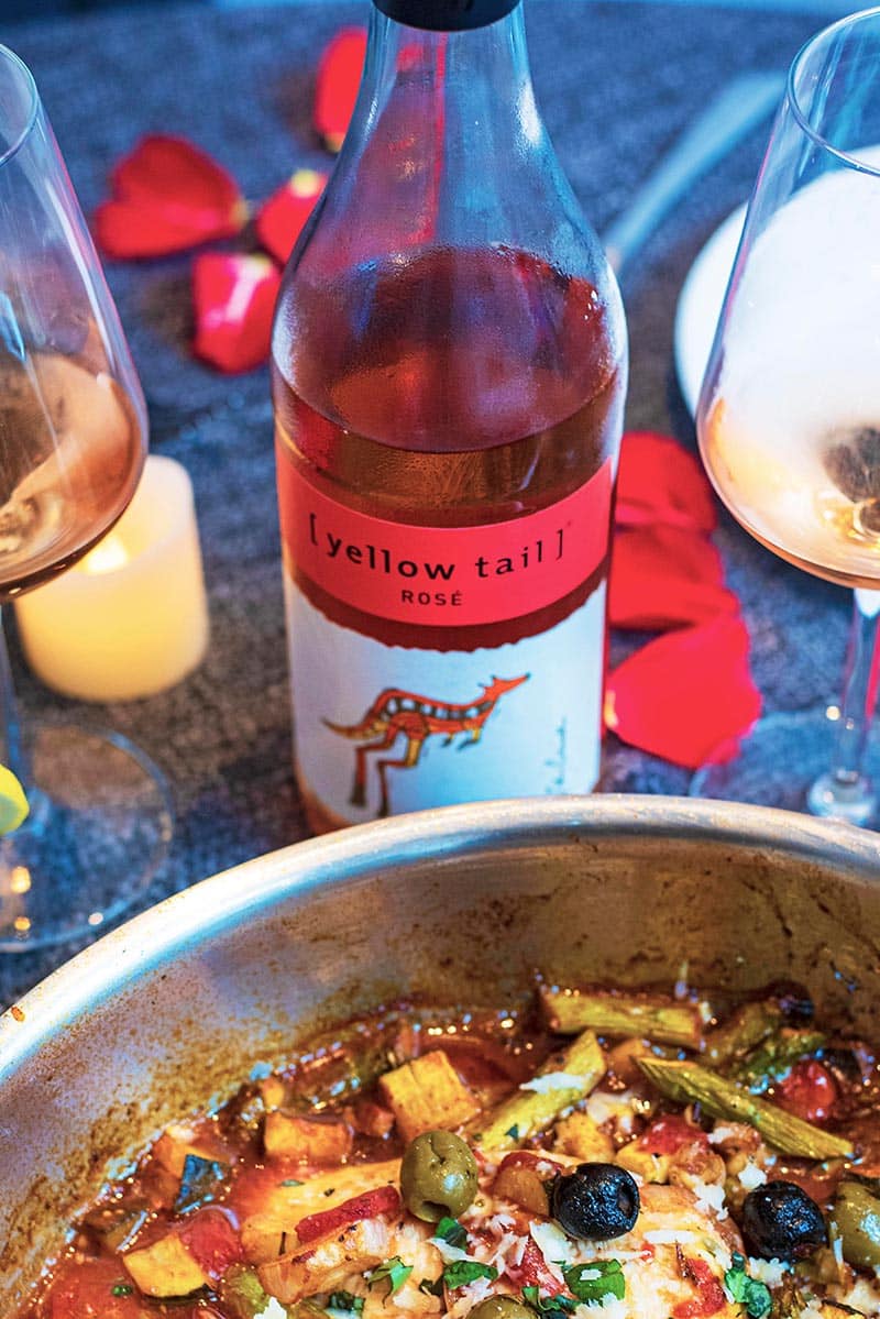 A bottle of Yellow Tail rosé wine next to a pan of chicken and vegetables.