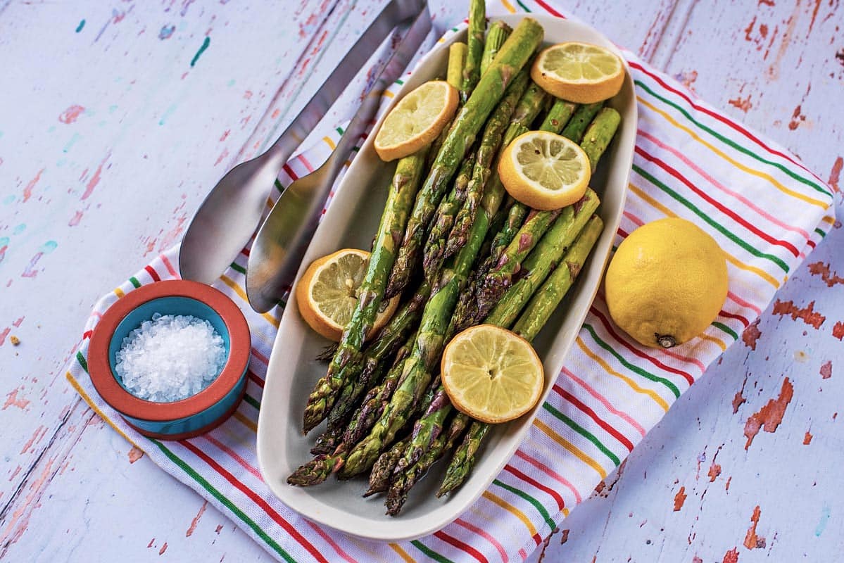 A plate of cooked asparagus and lemon slices on a plate sat on a striped towel
