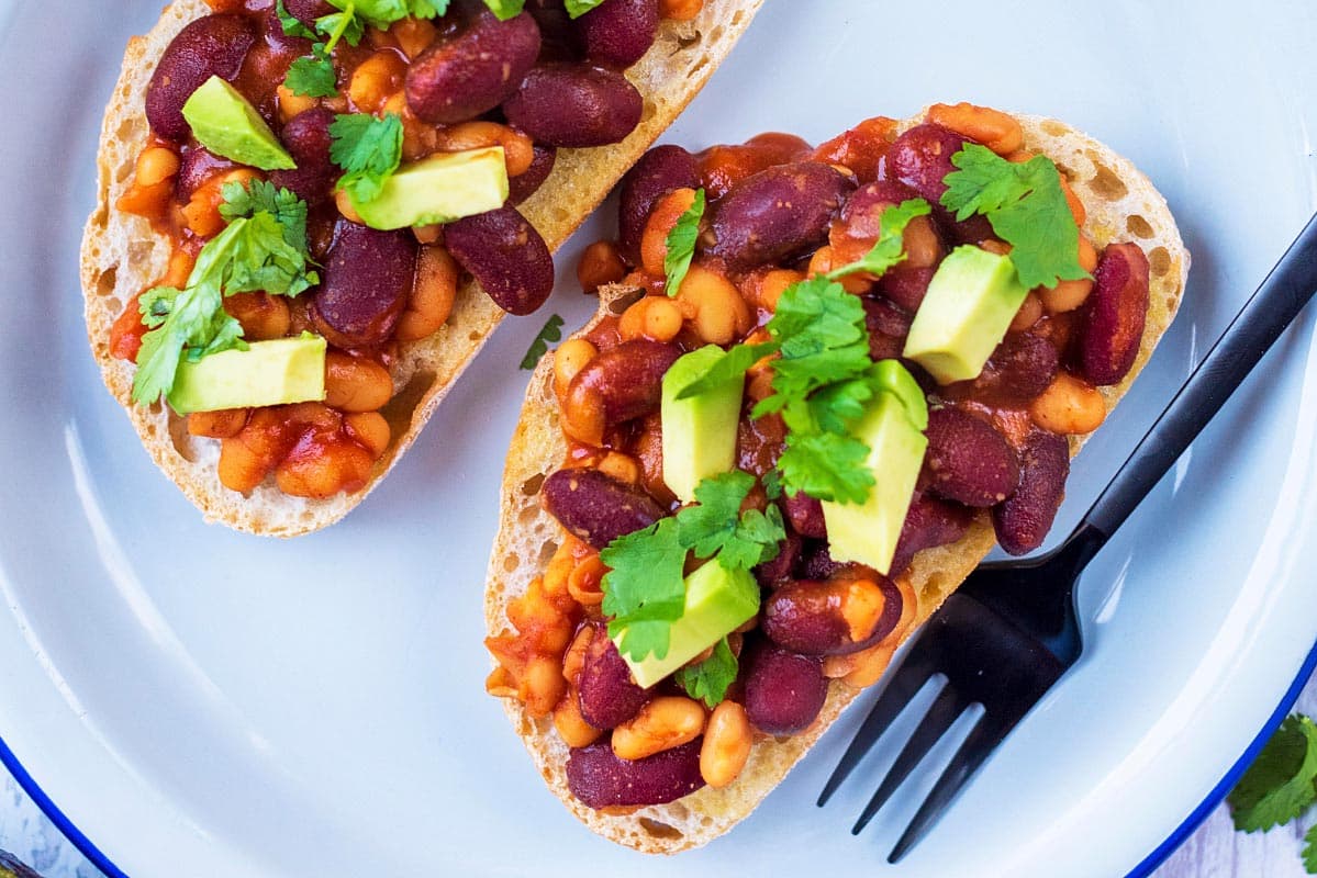 Two slices of toast, topped with beans and avocado.