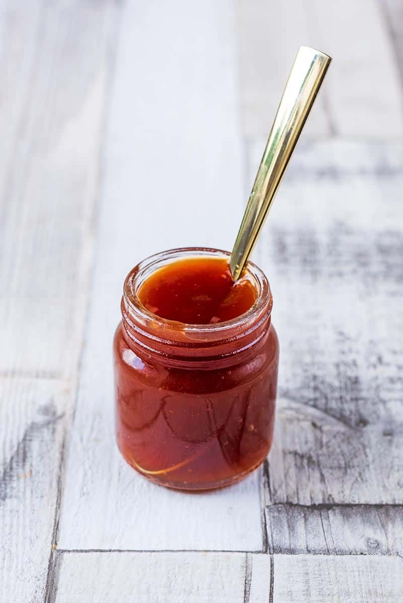 A small jar of sweet and sour sauce with a spoon sticking out of it
