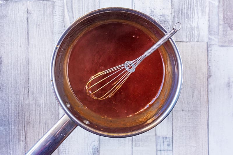 A saucepan containing sweet and sour sauce and a small whisk
