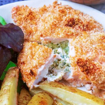 A chicken Kiev on a plate with salad and fries.