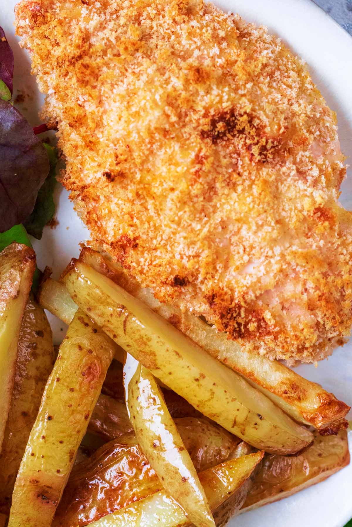 A baked chicken Kiev on a plate with some potato fries.