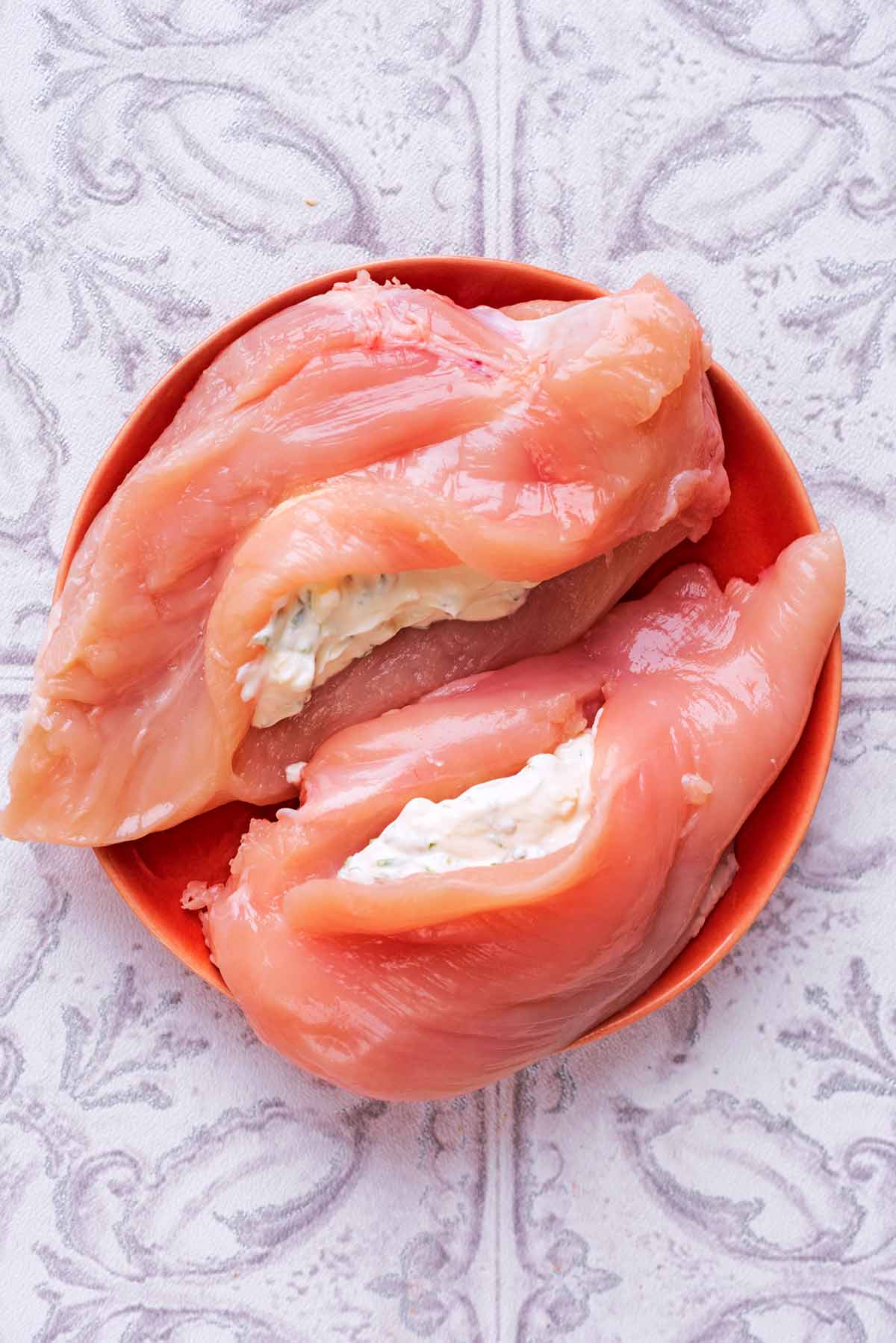 Two raw chicken breasts, sliced open and filled with a herby cheese filling.