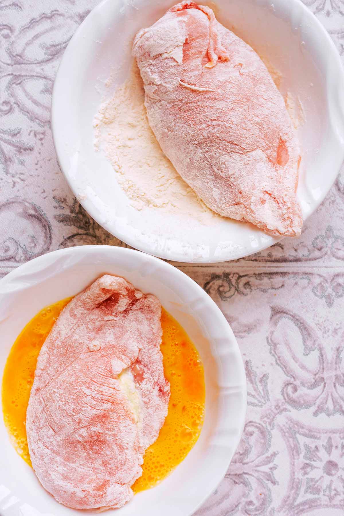 Two chicken breasts, both coated in flour, one in a bowl of beaten egg.