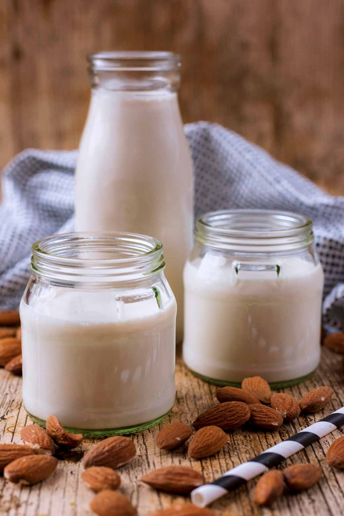 Almond milk in a milk bottle and two small jars. Almonds are scattered around.