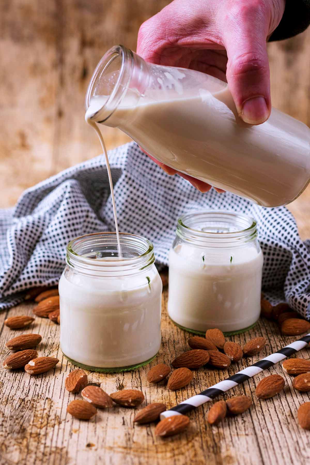 Someone pouring almond milk from a bottle into a small glass jar.