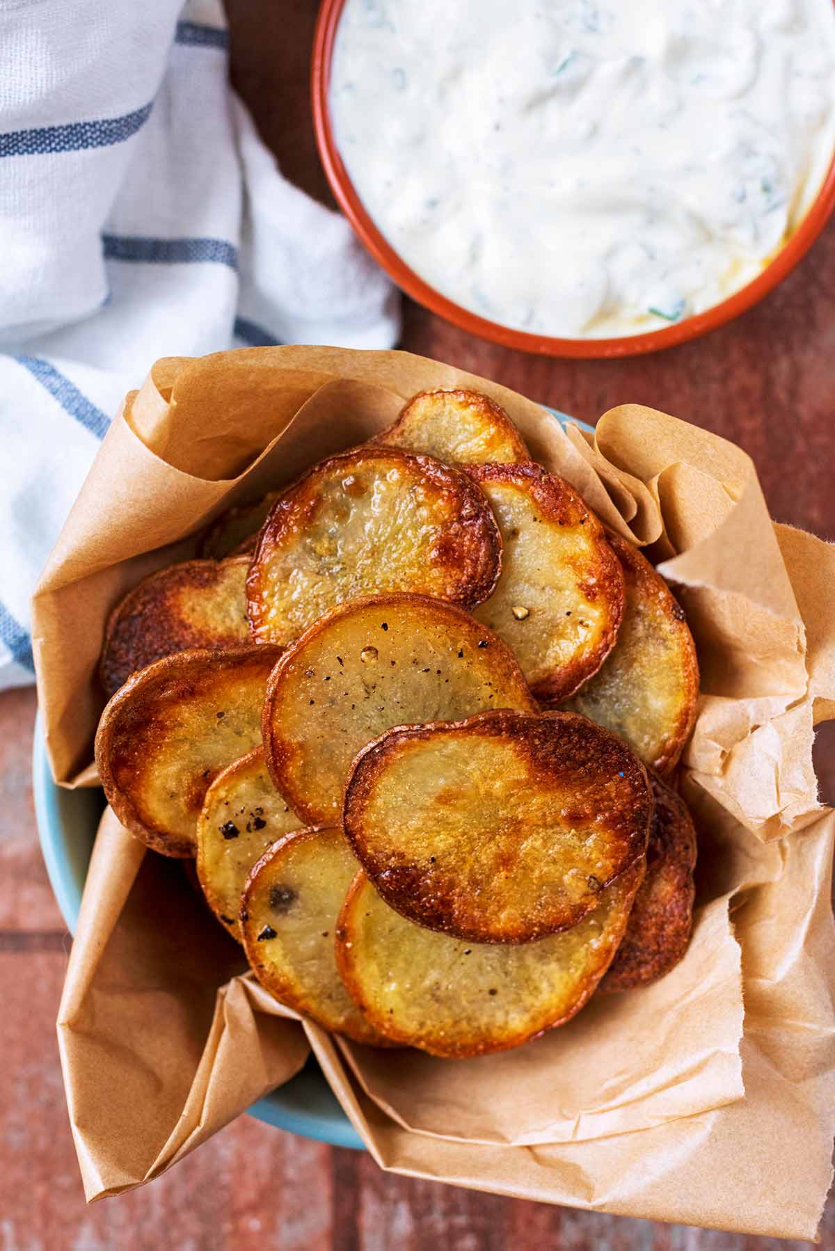 Homemade potato chips in a bowl next to some dip.