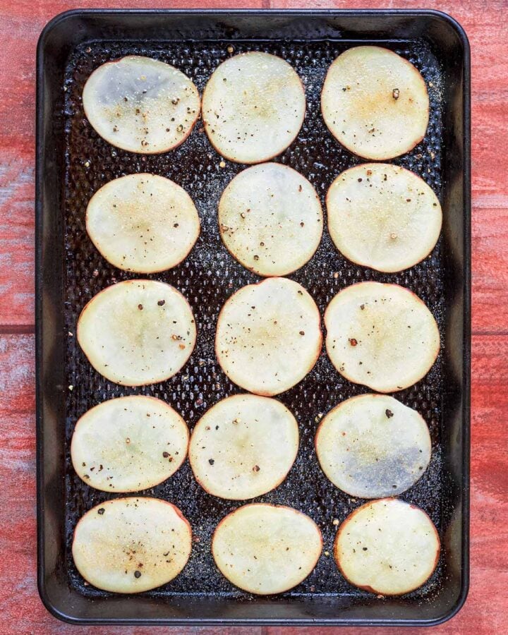 A baking tray with a layer of thinly sliced potatoes.
