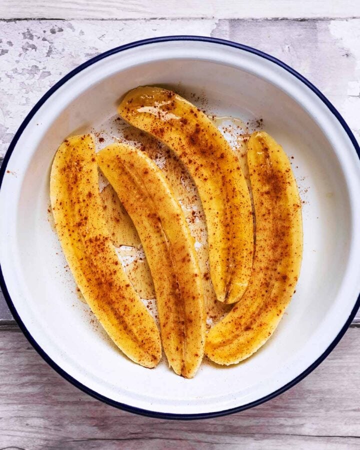 Four banana halves in a round dish covered in honey and cinnamon.