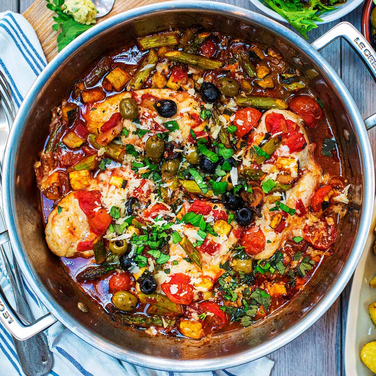 Italian Chicken in a large silver pan topped with chopped basil and parmesan shavings.